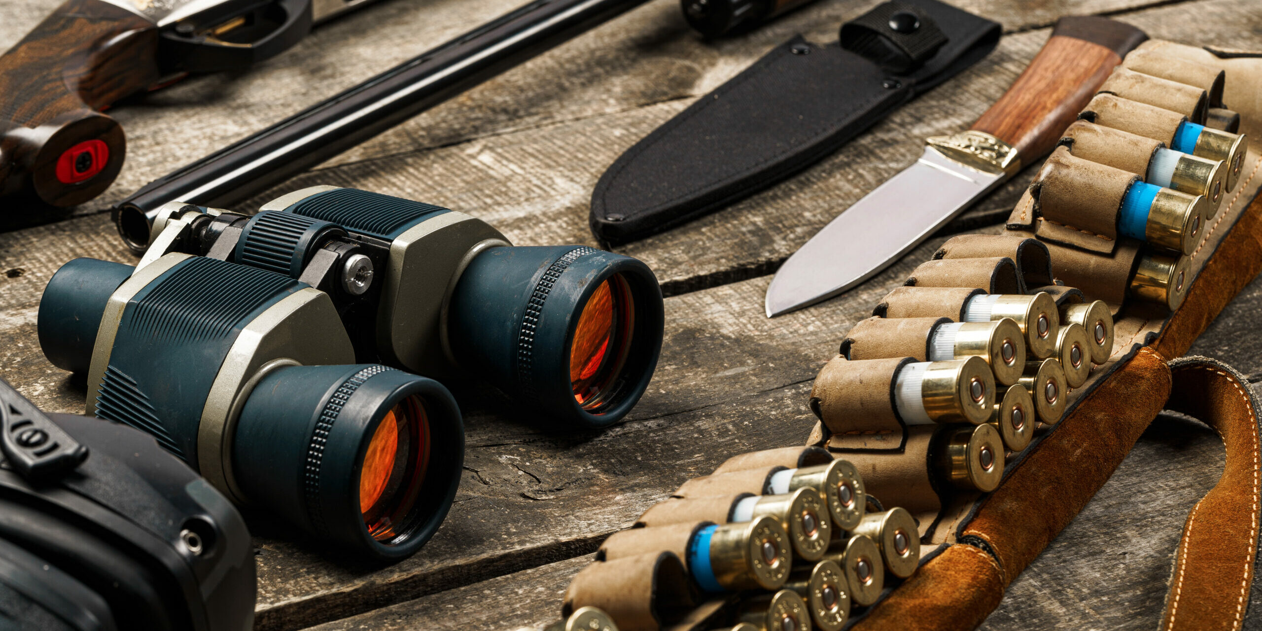 Hunting equipment on old wooden background including rifle, knife, binoculars and cartridges